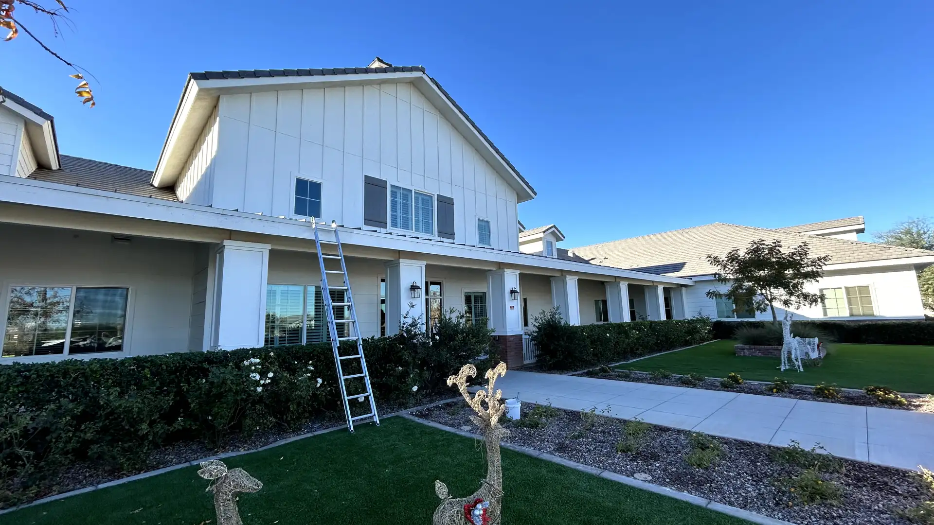 A large residential home with white siding and stucco, a ladder leaning against the porch, and holiday deer decorations on the lawn.