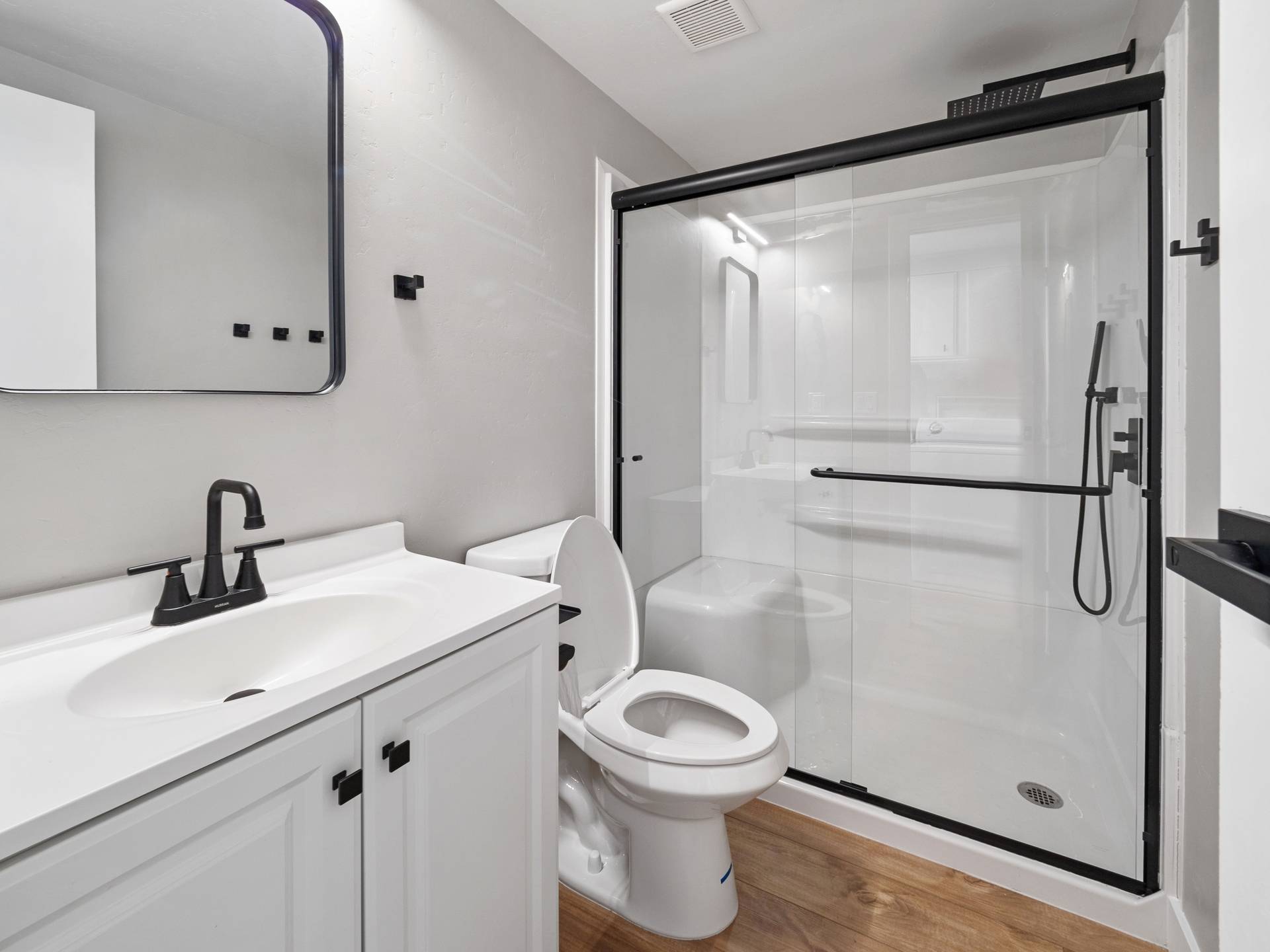 A modern bathroom with white vanity and sink, black fixtures, a white toilet, and a glass-enclosed shower with black trim.