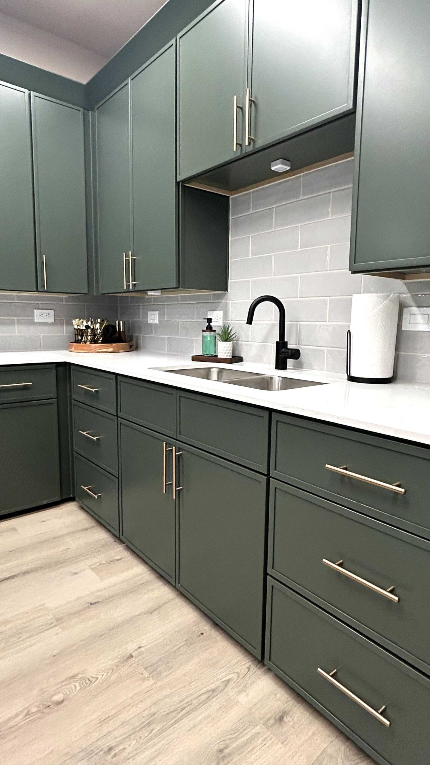 Modern kitchen with dark green cabinets, white countertops, and light gray subway tile backsplash.