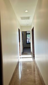 A freshly painted, long residential hallway with light walls, dark wood doors, and shiny tile flooring.