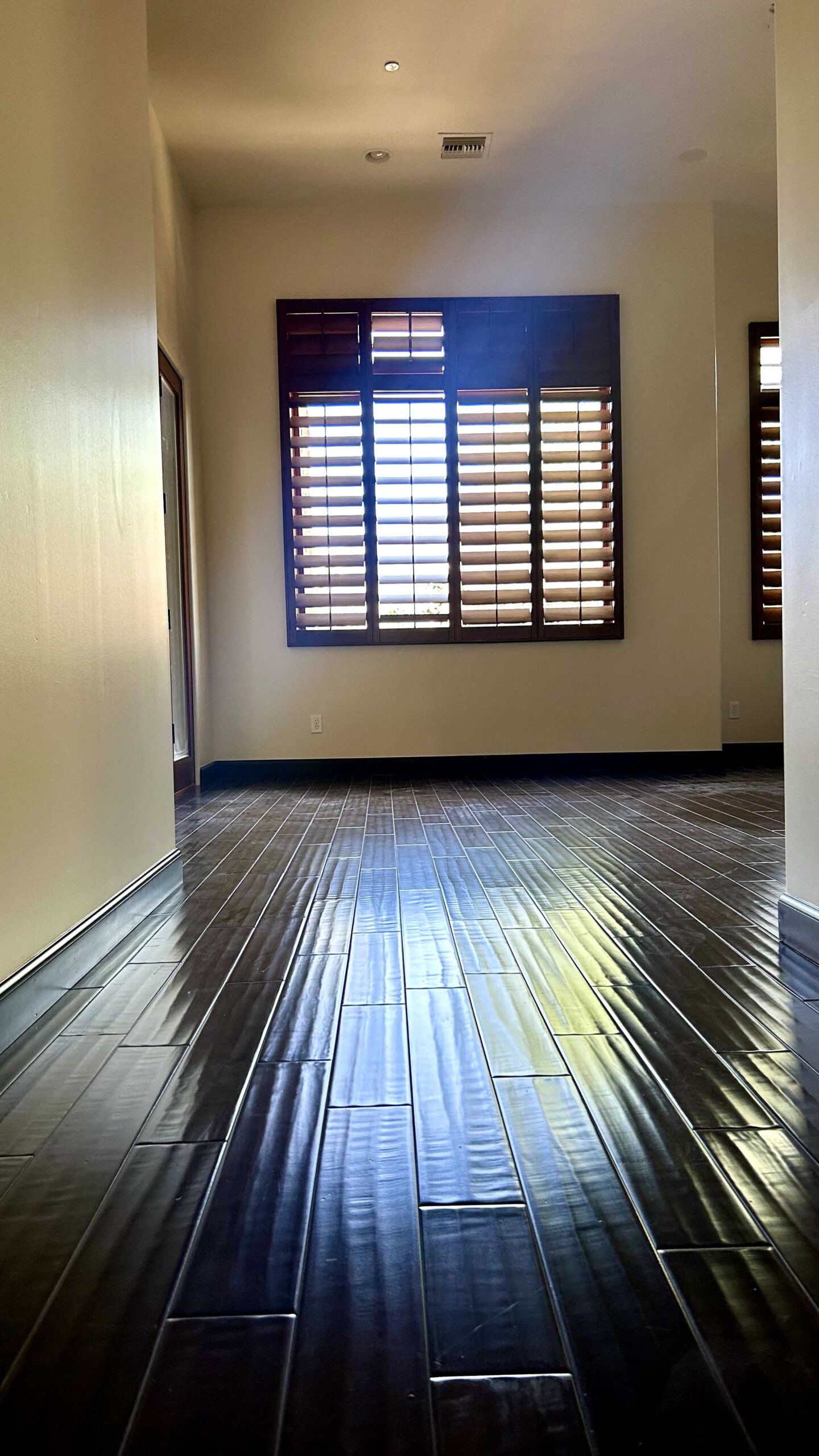 A residential hallway with gleaming dark wood floors, light painted walls, and windows with dark wood plantation shutters.