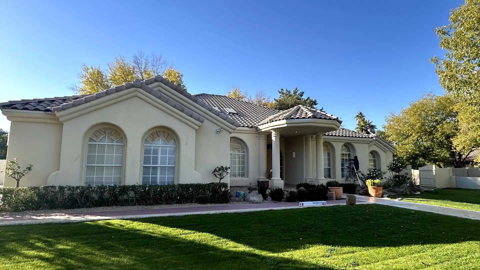 A large stucco home with arched windows, a covered entryway, and a green lawn under a clear blue sky.